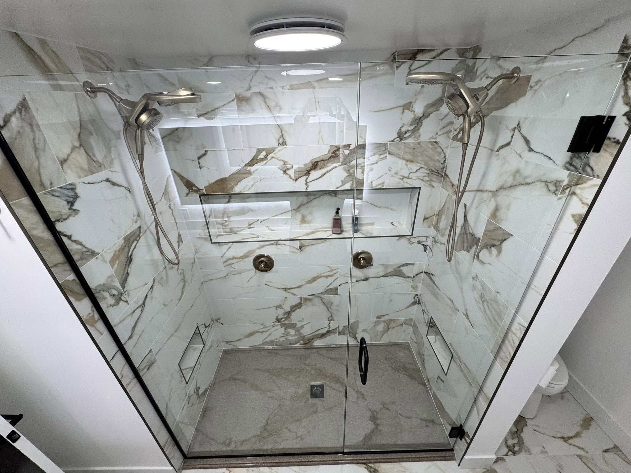 Walk-in shower finished in large-format veined marble tile with a glass enclosure and brushed gold fixtures