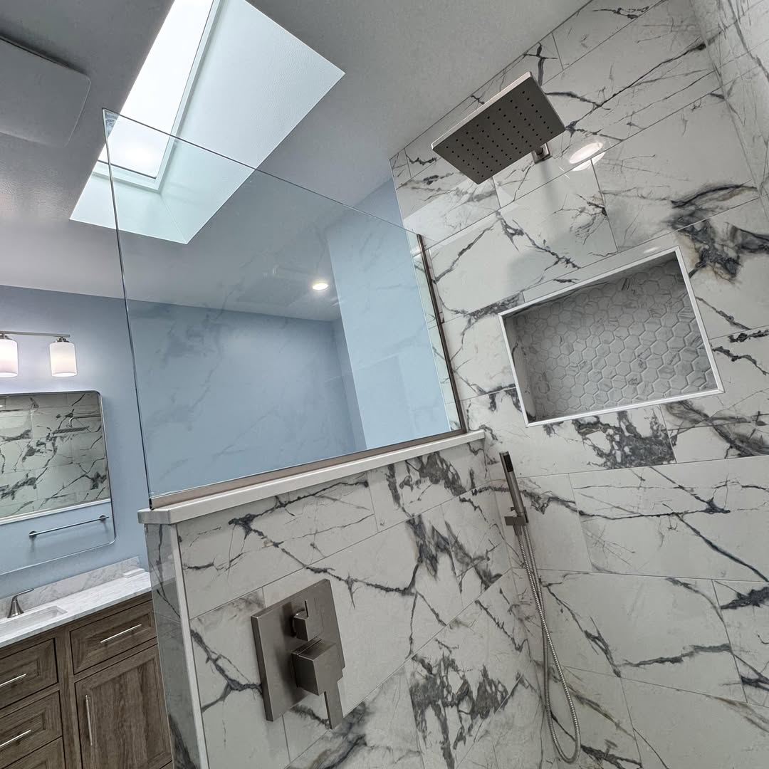 Marble-tiled shower with a built-in niche, glass door and a skylight above