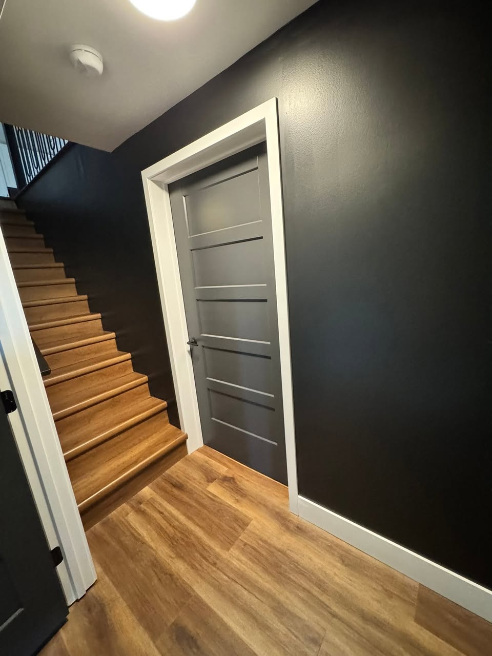 Finished lower level with a dark accent wall, hardwood flooring and an open staircase