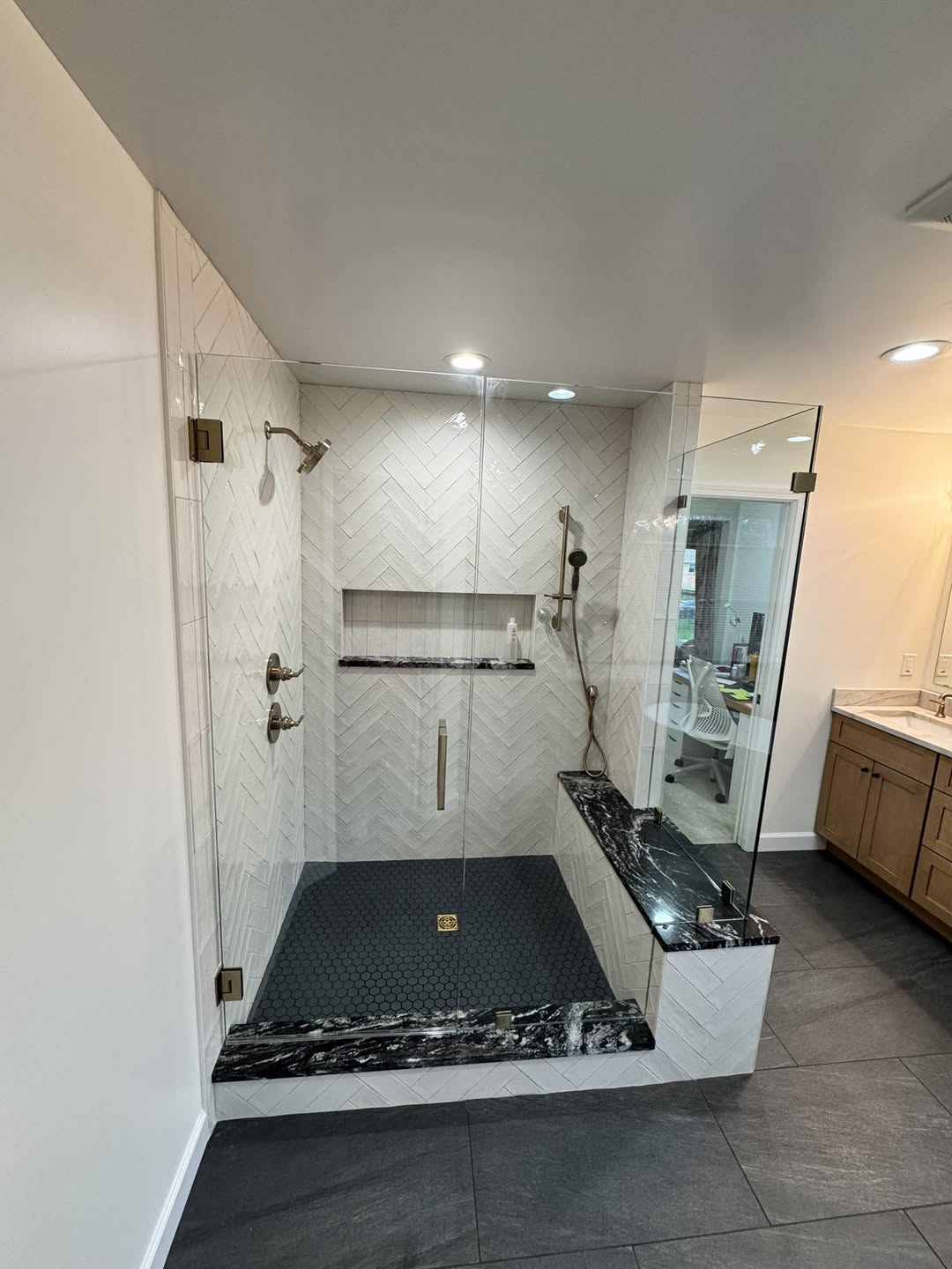 Walk-in shower in dark tile with a glass panel and a built-in bench
